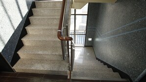 A staircase with granite steps and a wooden handrail, leading to a landing with a glass door. - The Core Albergue - Hostel (Seoul)