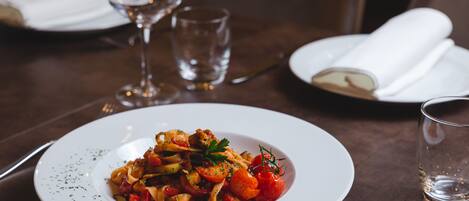 A dining table with a white plate of pasta, a glass of water, and a wine glass.