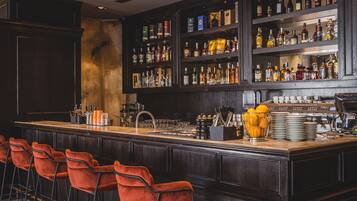 A bar area with a long counter, multiple shelves of liquor bottles, and several orange bar stools.