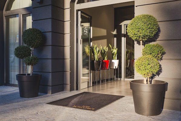 A modern building entrance with potted plants and a doormat. - Boscovich Boutique Hotel (Podgorica)