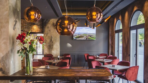 A restaurant with red chairs, a wooden table, and hanging spherical lights. - Boscovich Boutique Hotel (Podgorica)