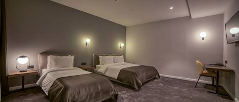 A modern hotel room with two beds, a desk, and a chair.