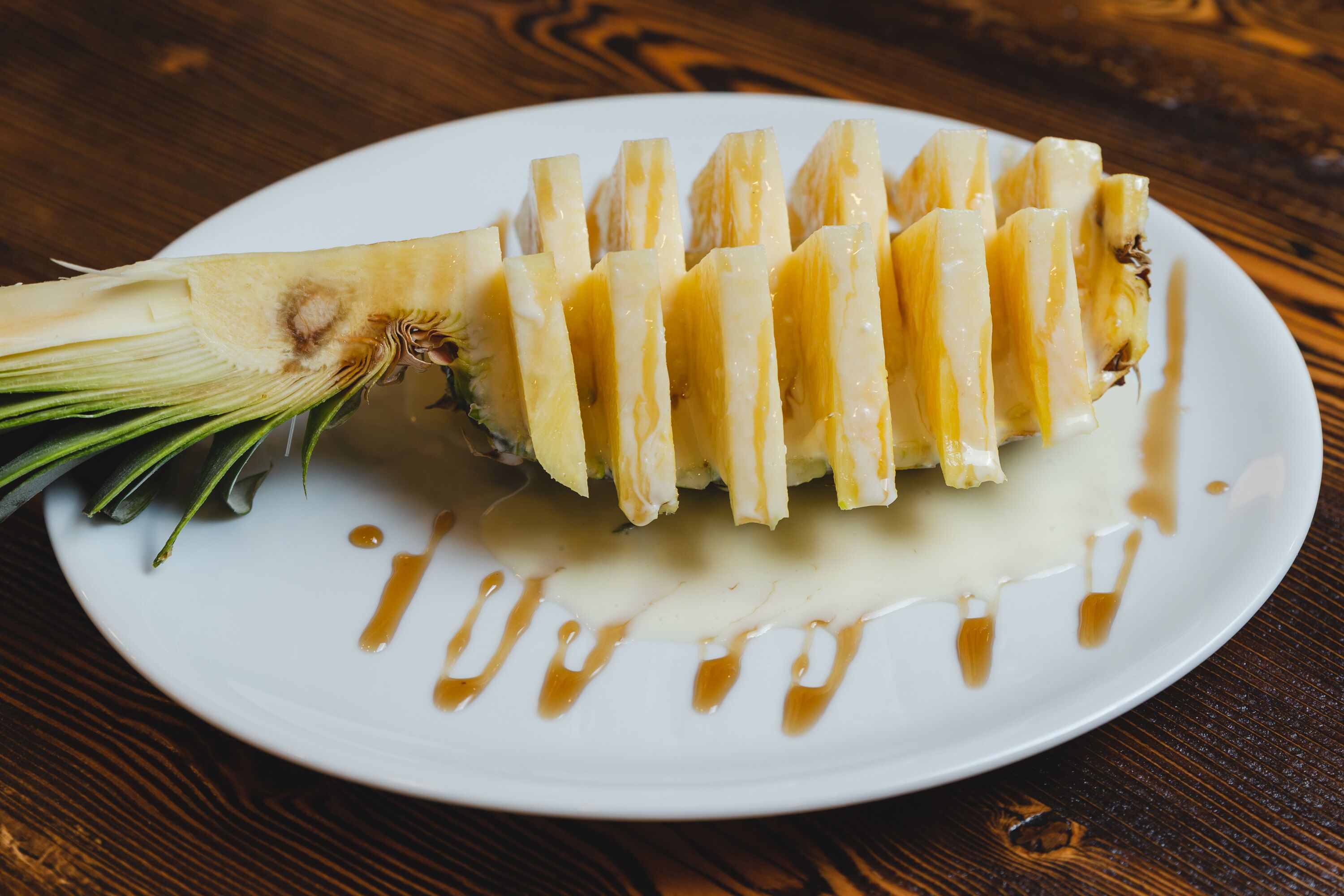 Une assiette blanche avec des tranches d’ananas et un filet de sauce, posée sur une table en bois.