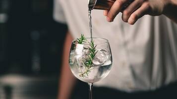 A person pouring a drink into a glass with ice and herbs.