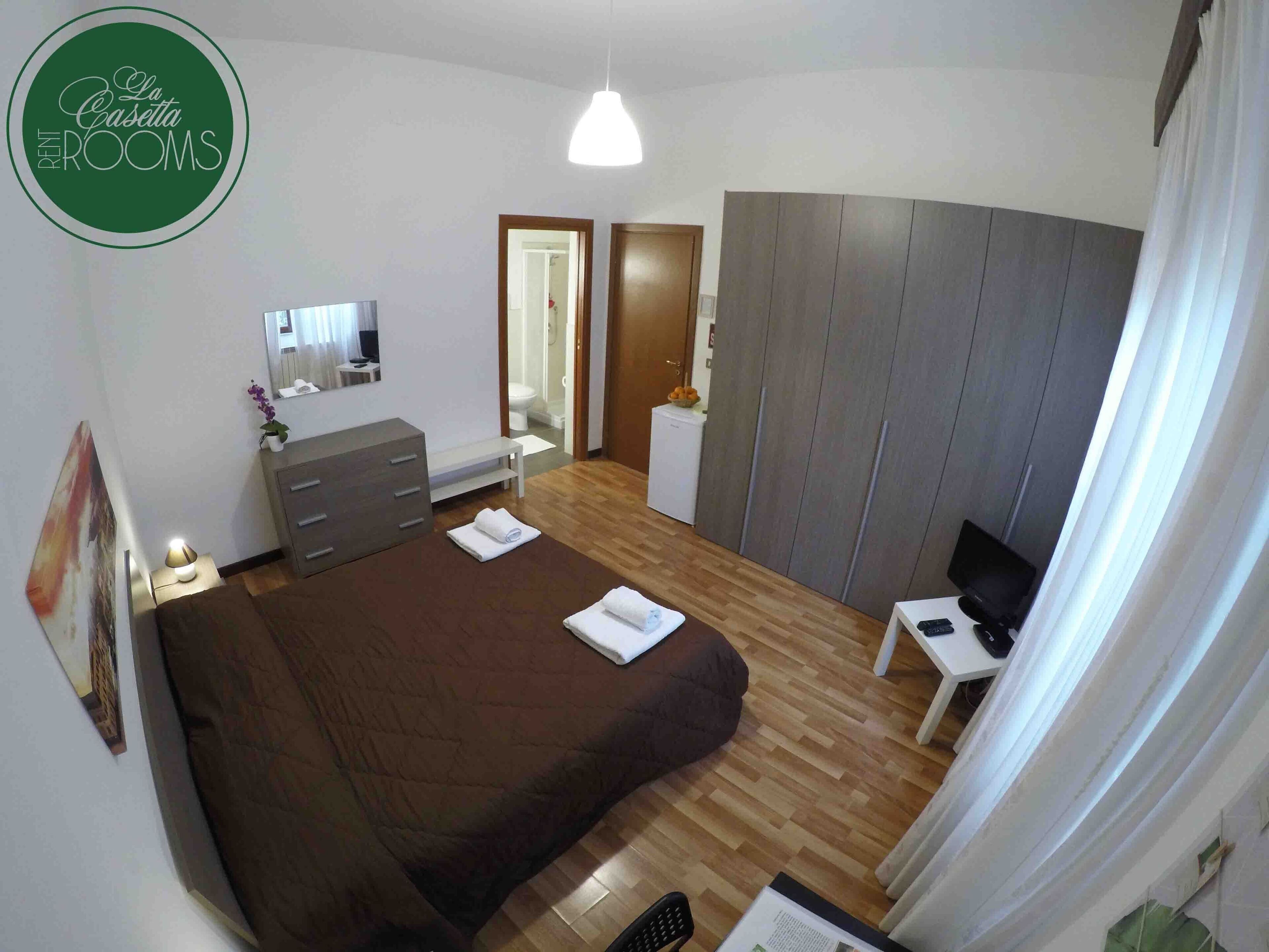 A bedroom with a bed, a desk, a wardrobe, a mirror, and a hanging light.