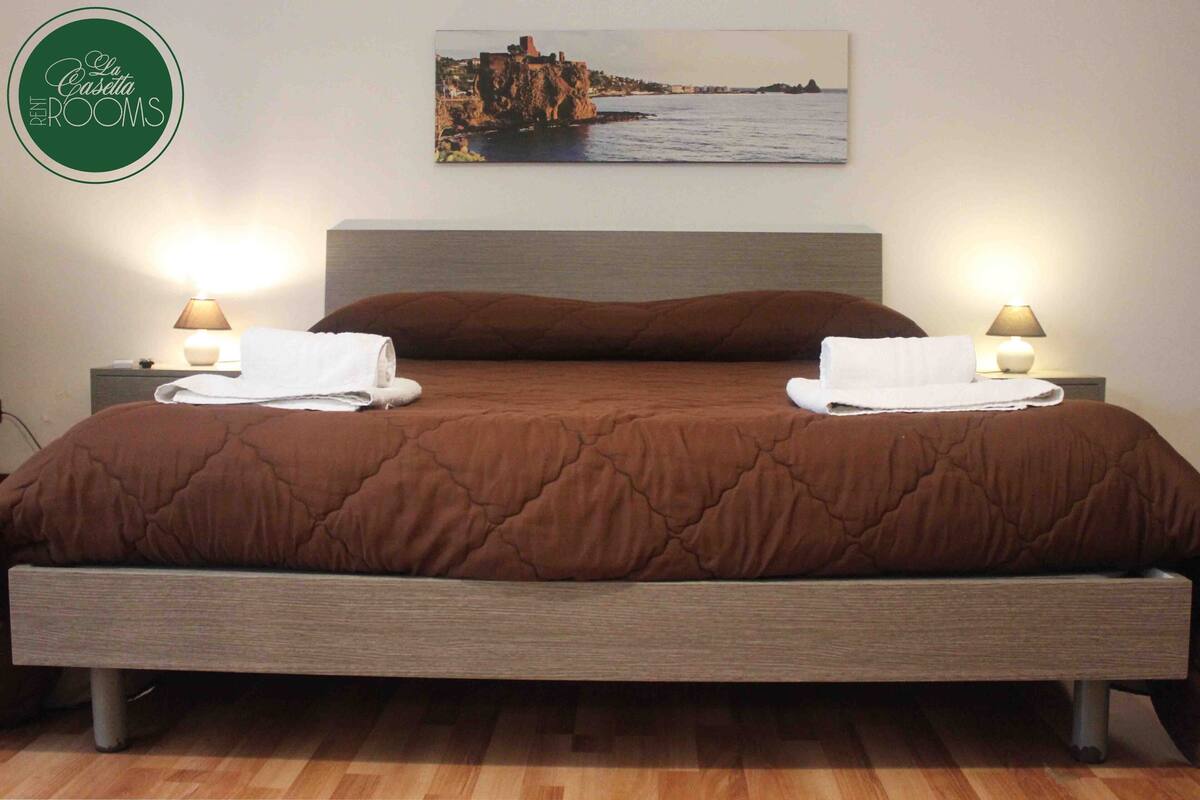 A neatly made bed with a brown quilt, two white towels, and two bedside lamps on wooden nightstands.