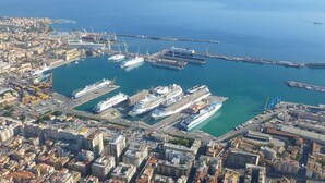 An aerial view of a port with multiple cruise ships docked, surrounded by urban buildings and a clear blue sky. - La Casetta (Palermo)