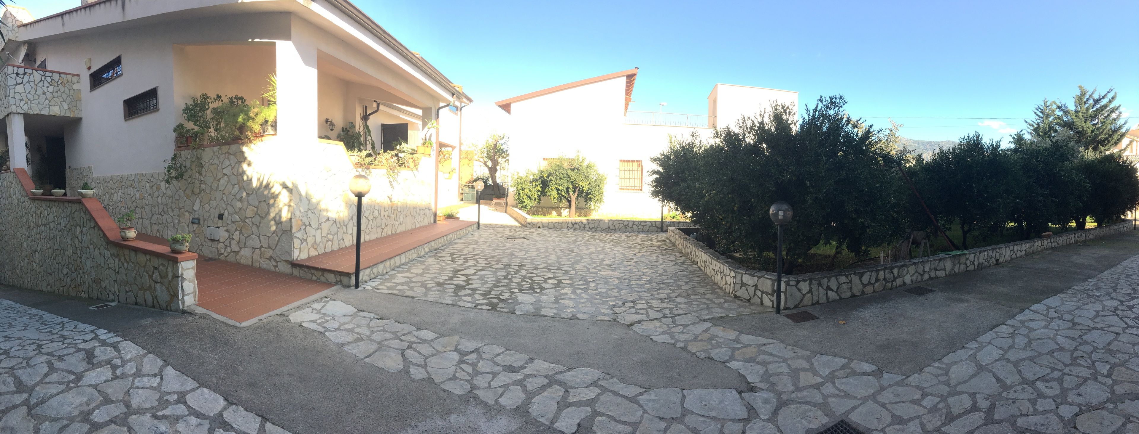 A residential area with stone-paved walkways, a house with a stone facade, and a clear sky.