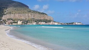 A coastal town with a beach, clear blue waters, and buildings along the shore. - La Casetta (Palermo)