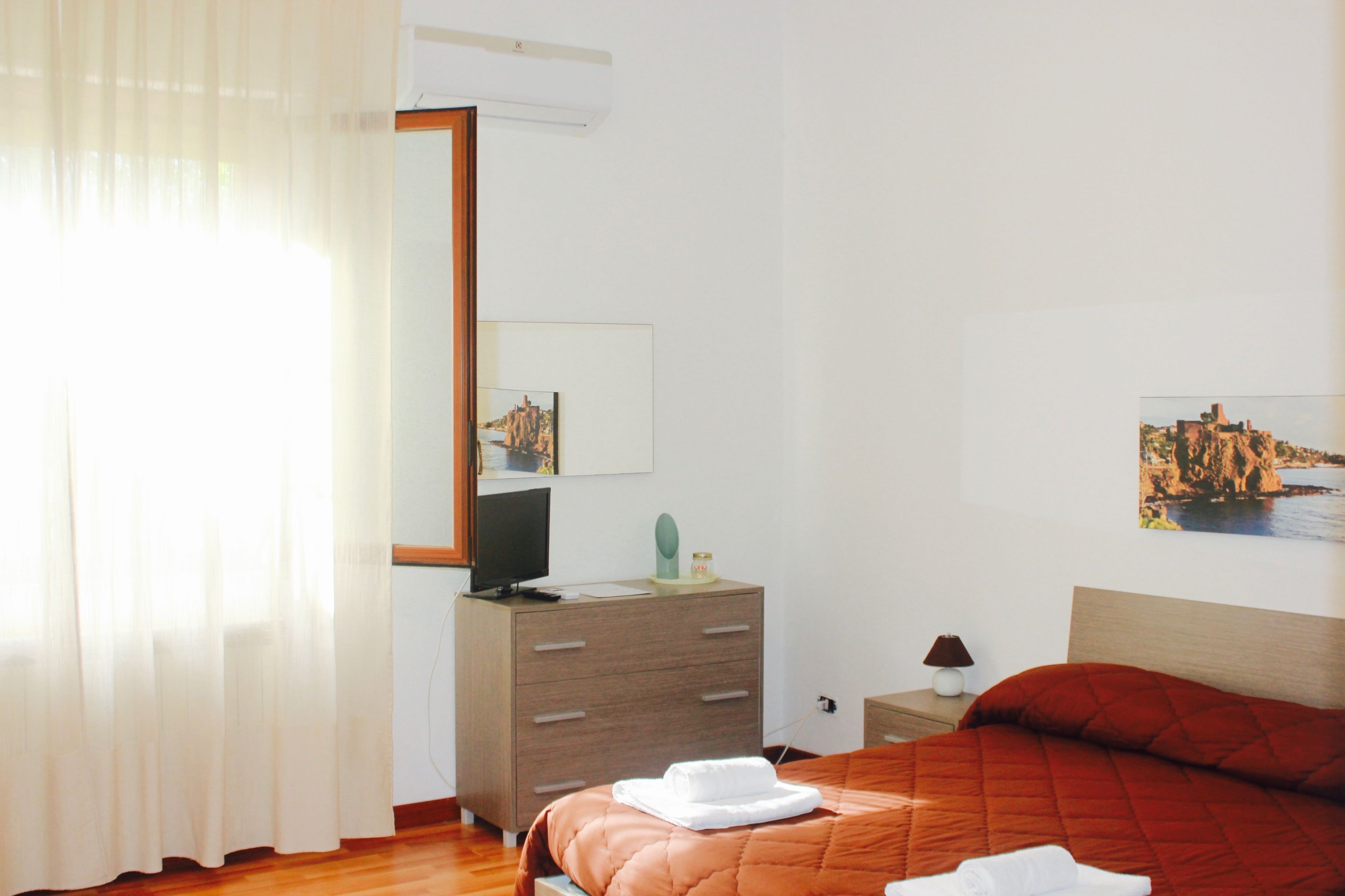 A hotel room with a bed, a dresser, a mirror, a television, and a painting on the wall.