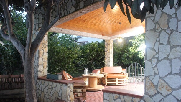 A covered outdoor seating area with stone walls and wooden furniture, including a table and chairs. - La Casetta (Palermo)