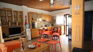 Eine moderne Küche mit Holzschränken, ein Essbereich mit orangefarbenen Stühlen und ein Fernseher im Wohnzimmer.
