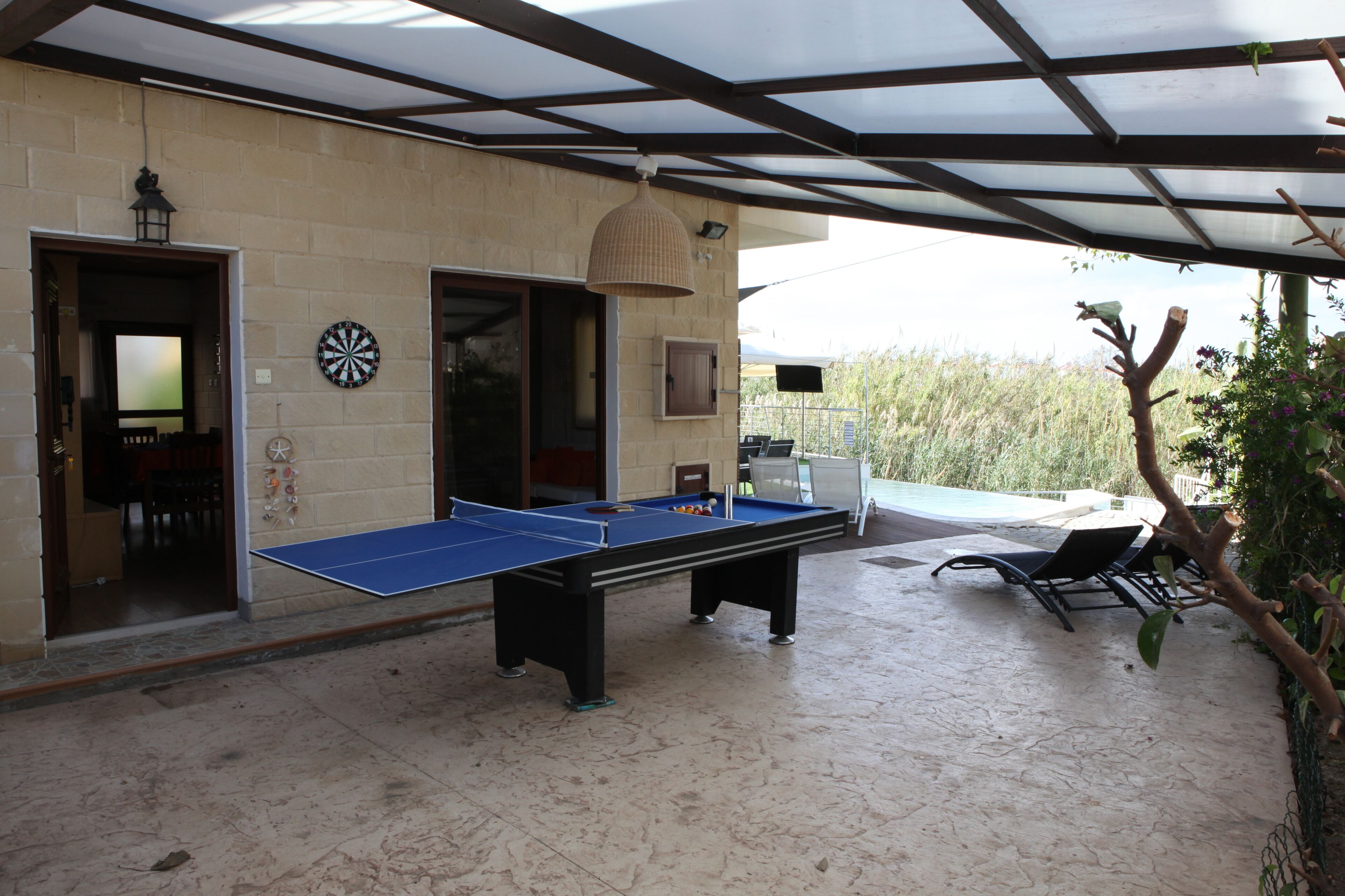 Une table de billard se trouve dans un espace extérieur abrité, avec un mur en pierre, une porte et une chaise.