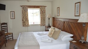A neatly made bed with a wooden headboard, a bedside table with a lamp, a chair, and a window with curtains.