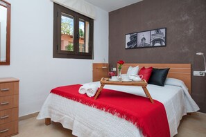 A neatly made bed with a red and white bedspread, a wooden headboard, and a bedside table with a tray of toiletries.