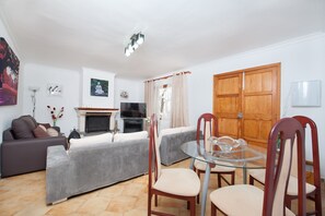 A living room with a sofa, a glass table, and chairs. There is a television and a fireplace.