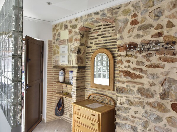 A room with a stone wall, wooden furniture, a mirror, and a hanging coat rack.