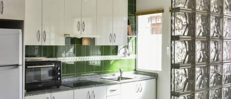 A modern kitchen with white cabinets, a microwave, and a green backsplash.
