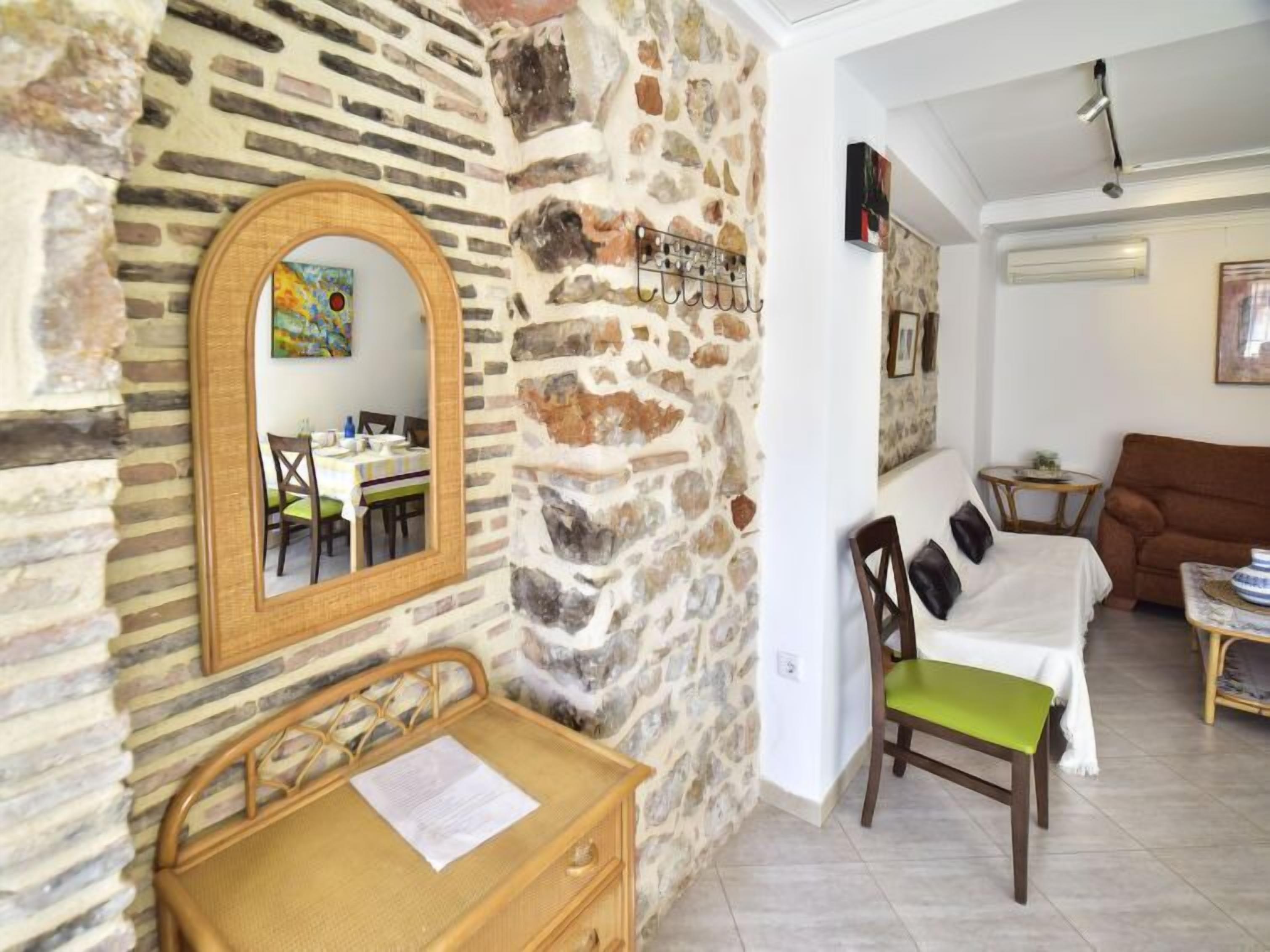 Una stanza con parete in pietra, una scrivania in legno, una sedia, un letto e un tavolino con una ciotola.
