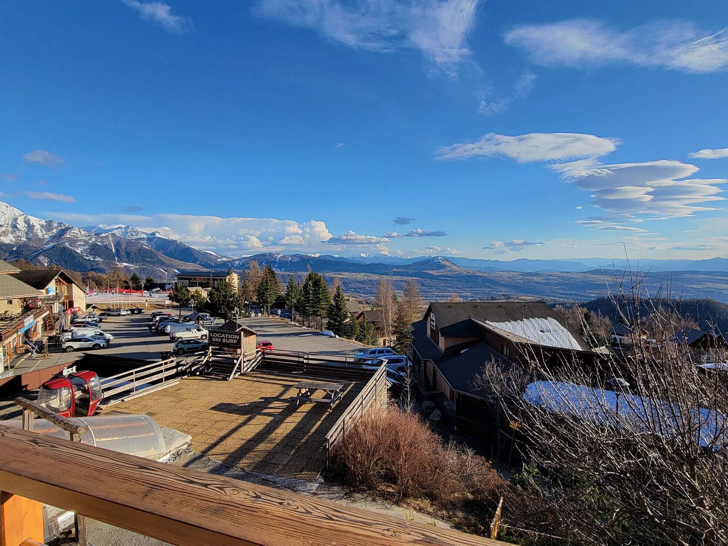 Ein Skigebiet mit Parkplatz, Gebäuden und Blick auf schneebedeckte Berge.