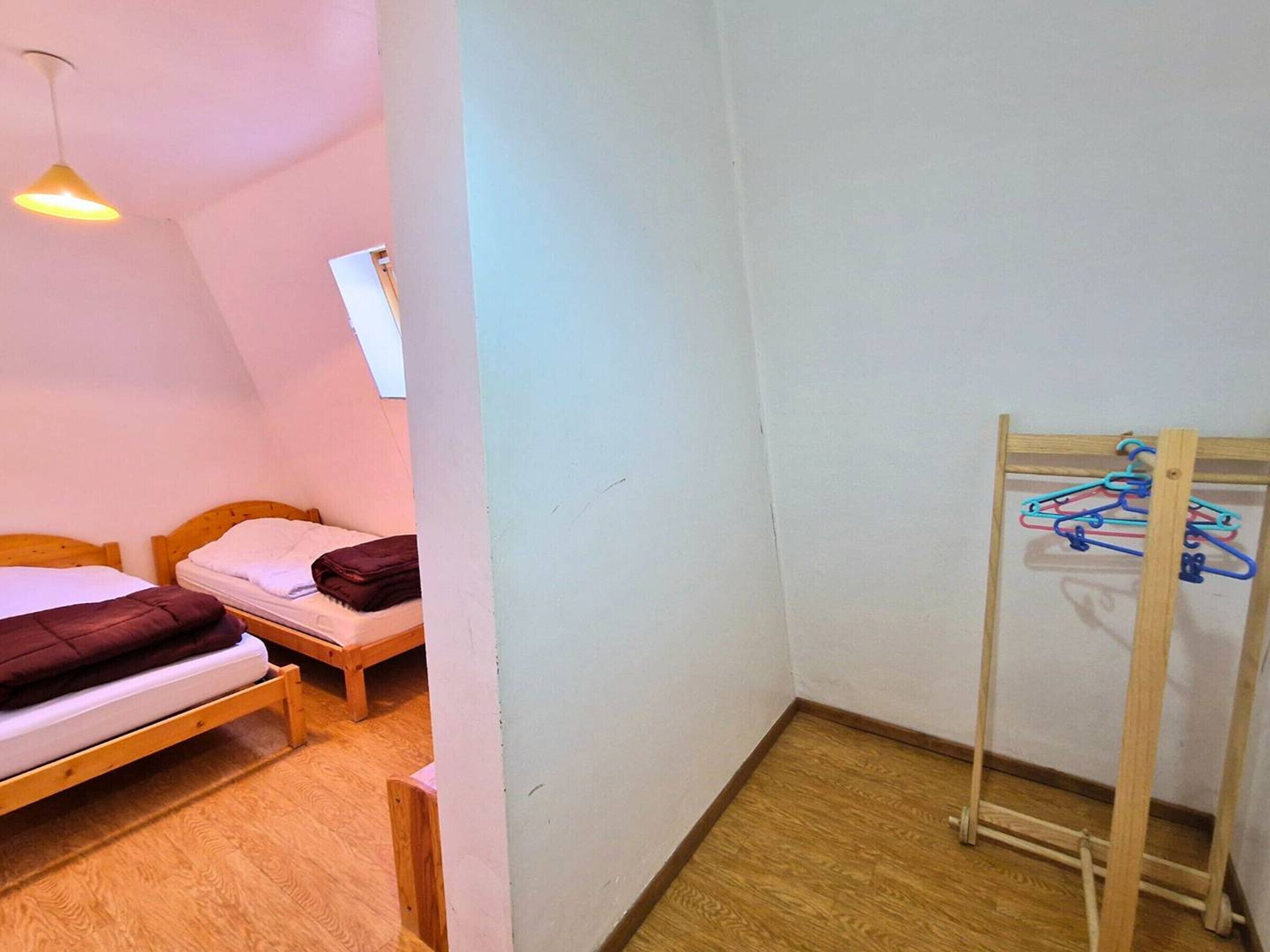 Et lille, hyggeligt rum med to træsenge, et træklædestativ med bøjler og en enkelt pendel.