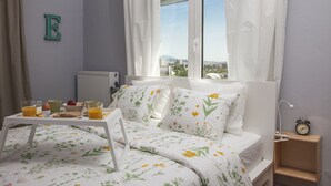 A bedroom with a bed, a bedside table with a lamp, a clock, and a window with curtains. - Sunny & Happy Apartment Historic Center (Thessaloniki)