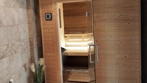 Een houten sauna met een glazen deur, een klein bedieningspaneel aan de muur en een bankje binnen.
