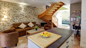 Een woonkamer met een stenen muur, een bruine bank, een houten salontafel met fruit, en een trap naar een andere kamer.