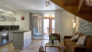 Een moderne keuken met een centraal eiland, een eethoek met tafel en stoelen, en een woonkamer met een bank en decoratieve kussens.