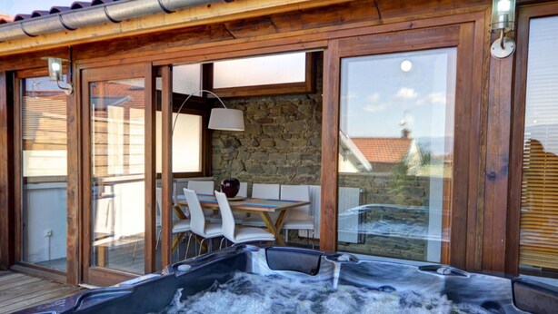 Een hottubgedeelte met een houten terras, een stenen muur en een tafel met stoelen.