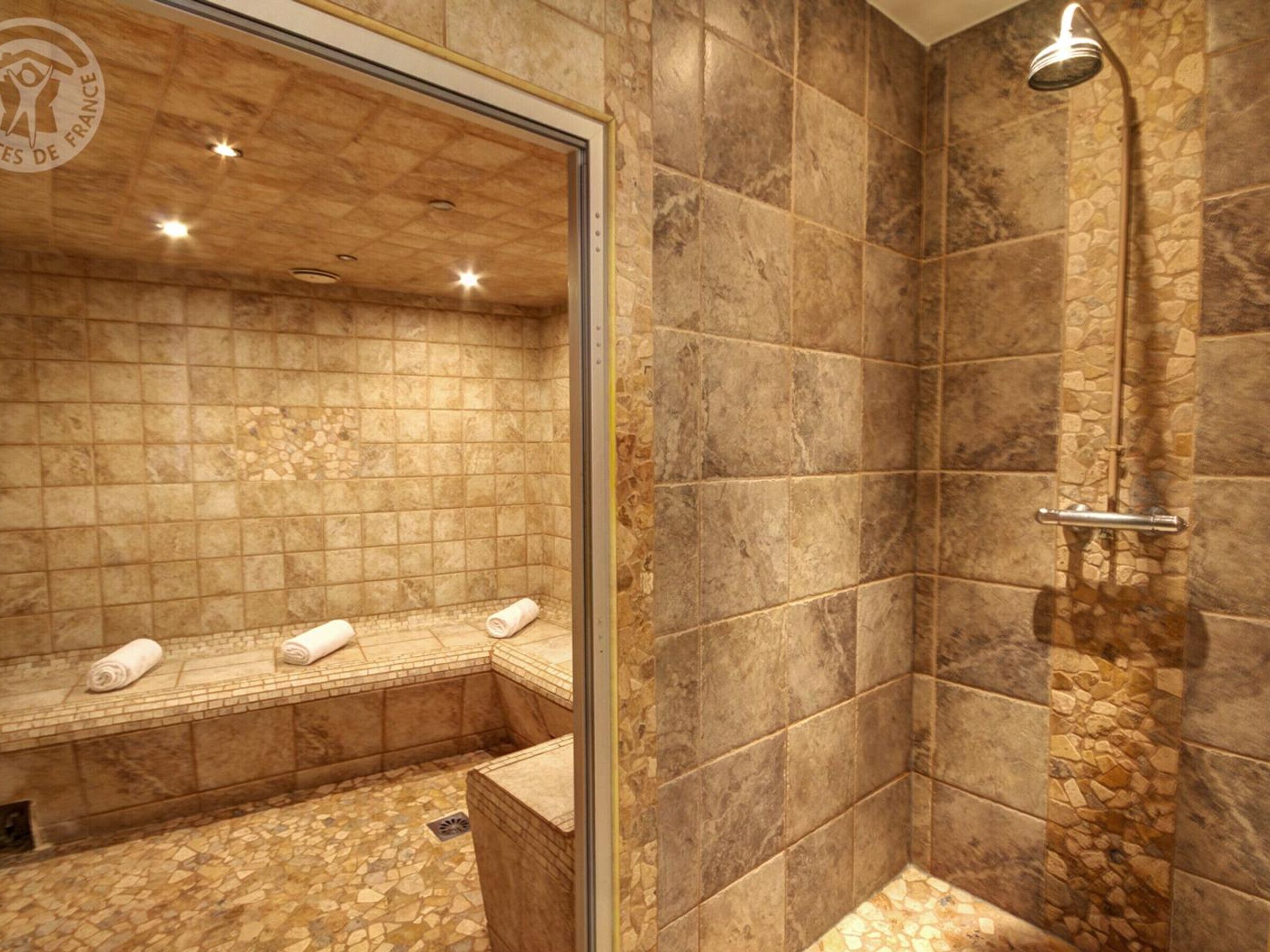 A modern bathroom with a stone-tiled shower, a bench with towels, and a glass-enclosed area.