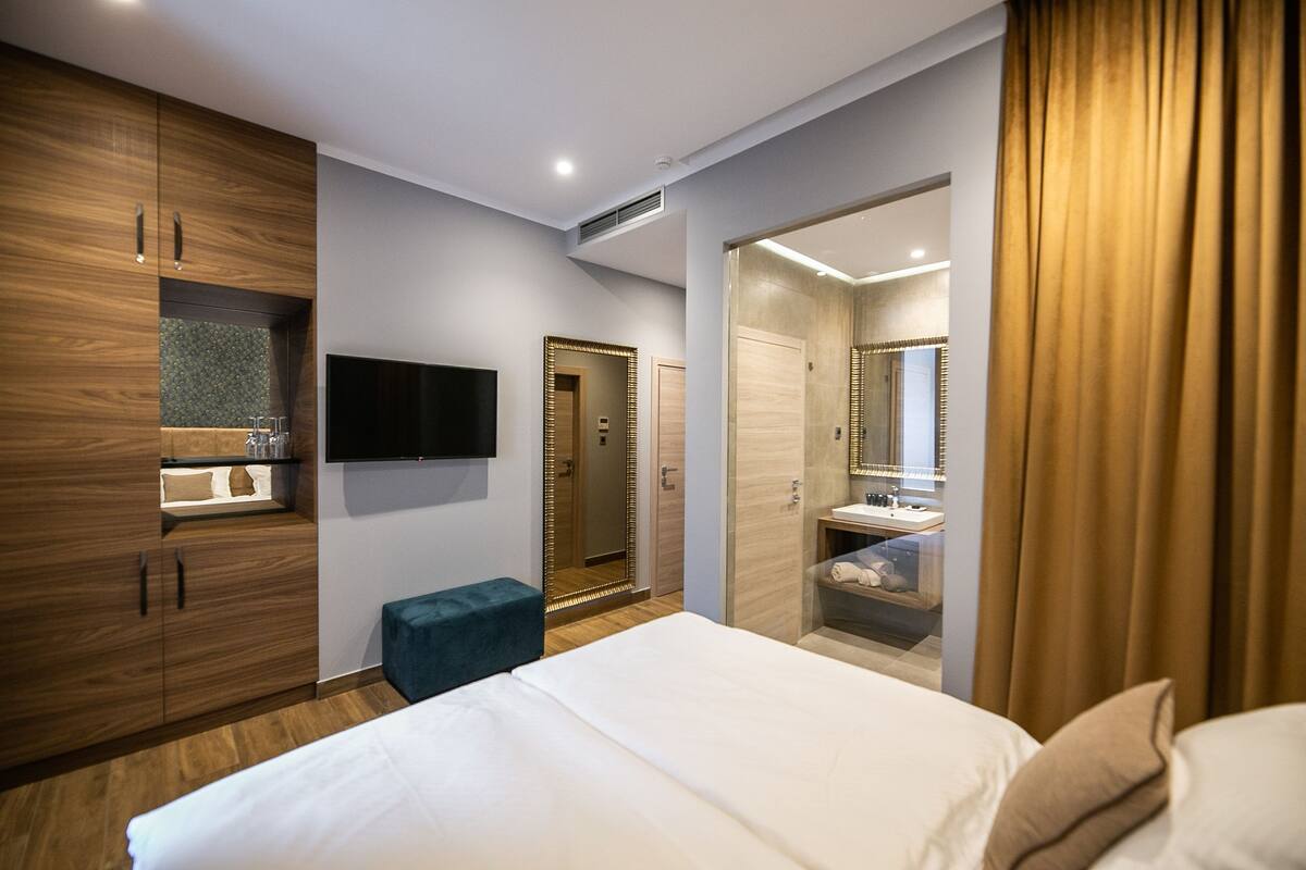 Een moderne hotelkamer met een groot bed, een houten garderobe, een televisie, een badkamer met een spiegel en een douche.