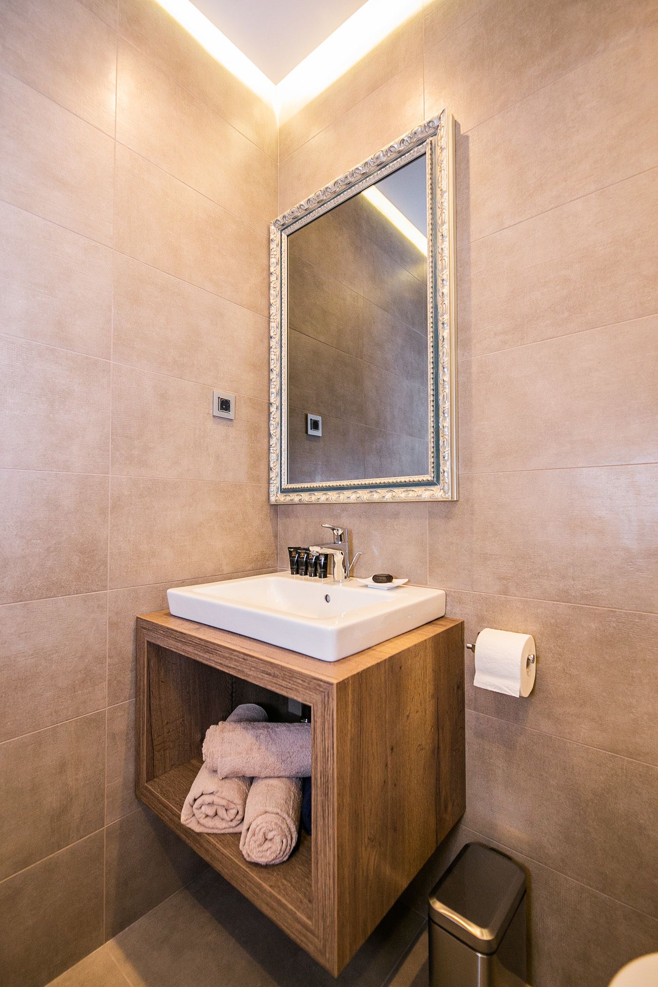 Ein modernes Badezimmer mit einem Holzbadezimmerhocker, einem großen Spiegel und einer eingebauten Ablage für Handtücher.