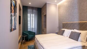 A modern hotel room with a large bed, a green armchair, a small side table, and a large window with curtains.