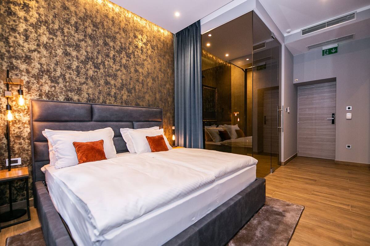 Een moderne hotelkamer met een groot bed, een nachtkastje, een spiegel en uitzicht op de gang.