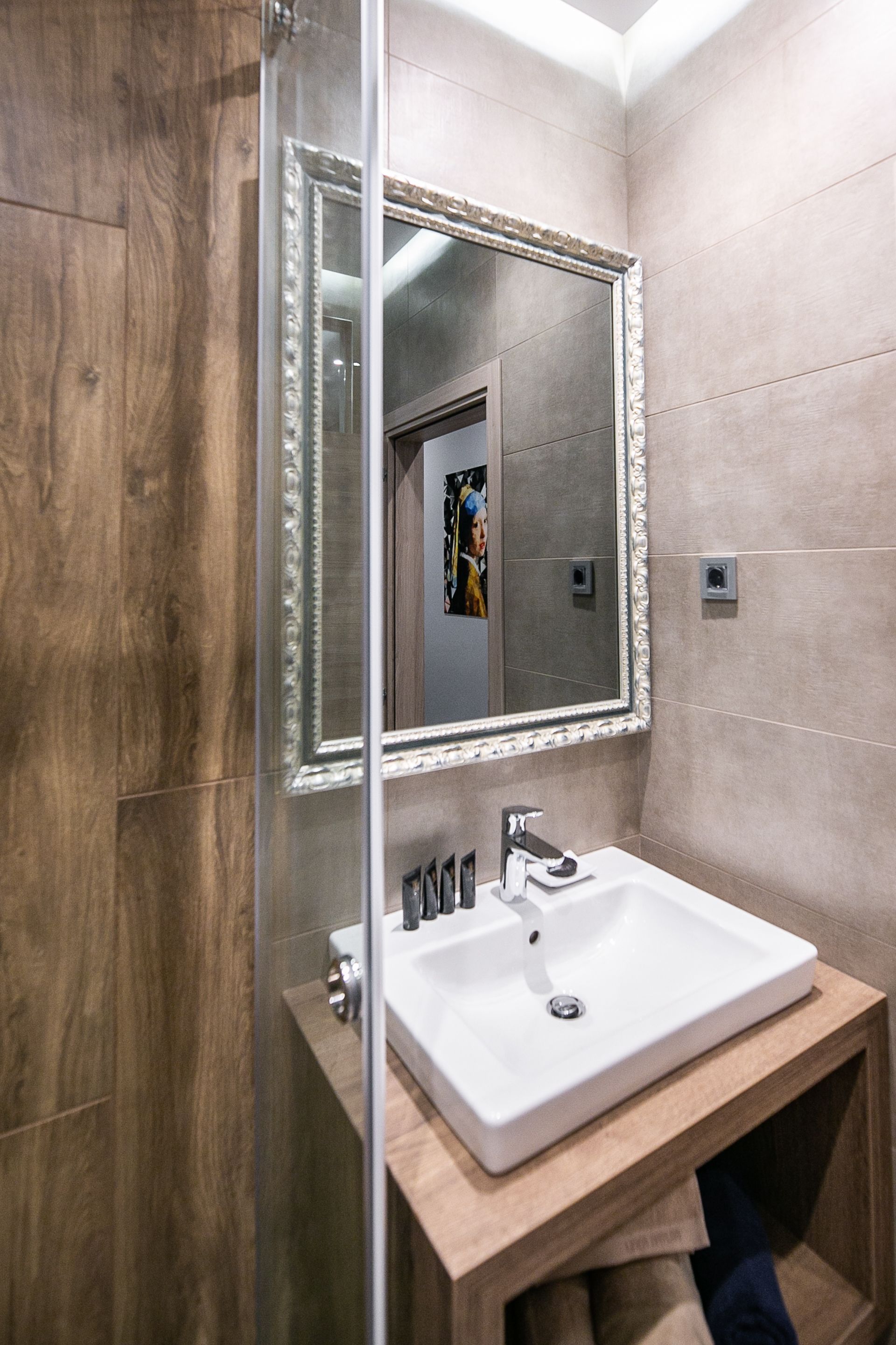 A bathroom with a wooden vanity, a white sink, and a large mirror with a decorative frame.
