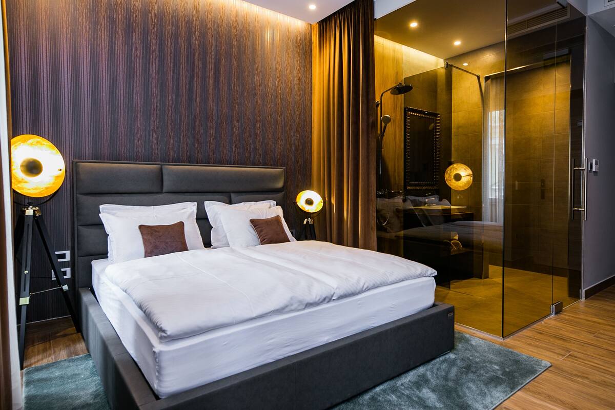 Een moderne slaapkamer met een groot bed, donker houten lambrisering en een douchecabine met glazen wanden.