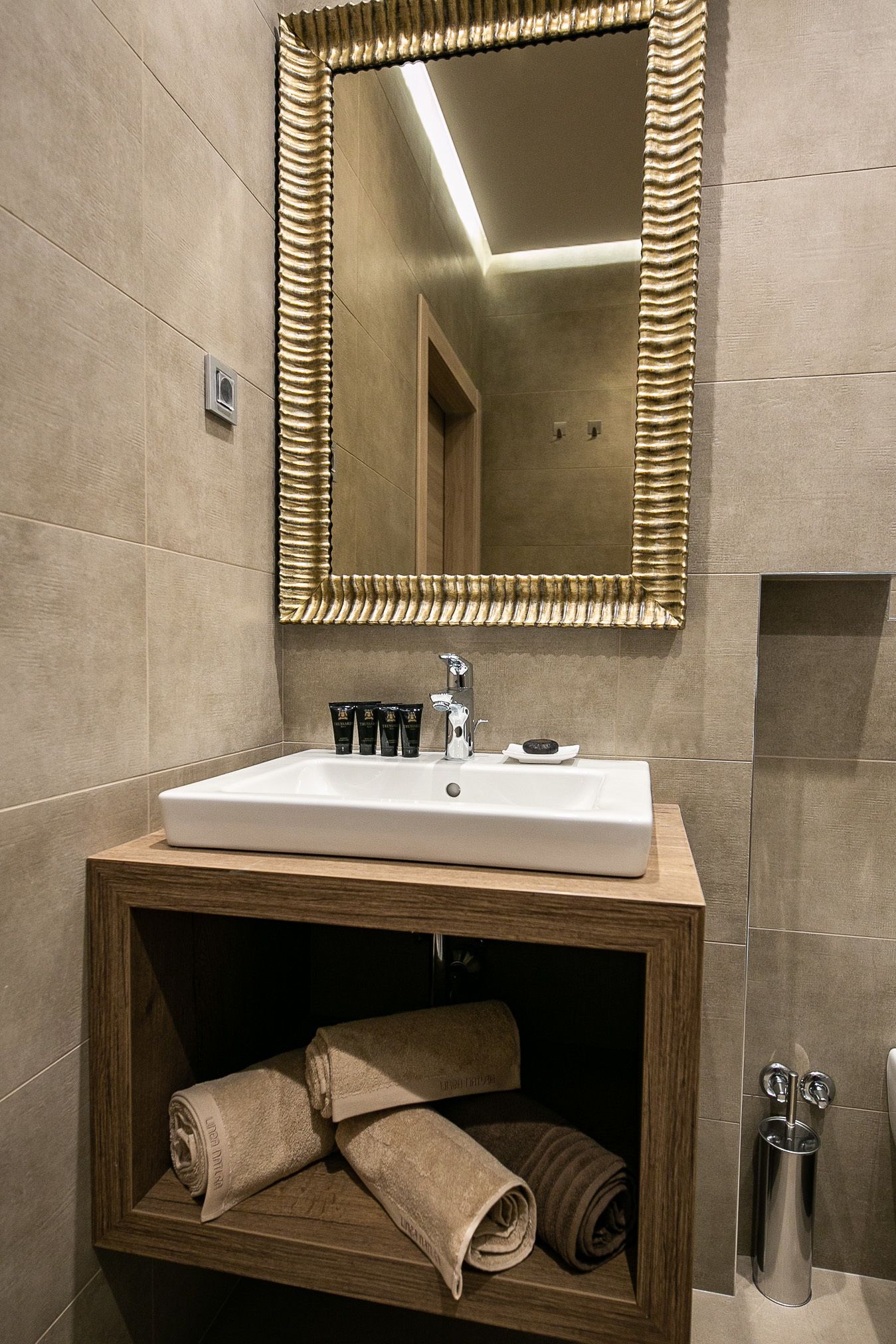 Une salle de bain avec un lavabo blanc, un miroir doté d’un cadre texturé et un meuble-lavabo en bois sur lequel sont posées des serviettes.