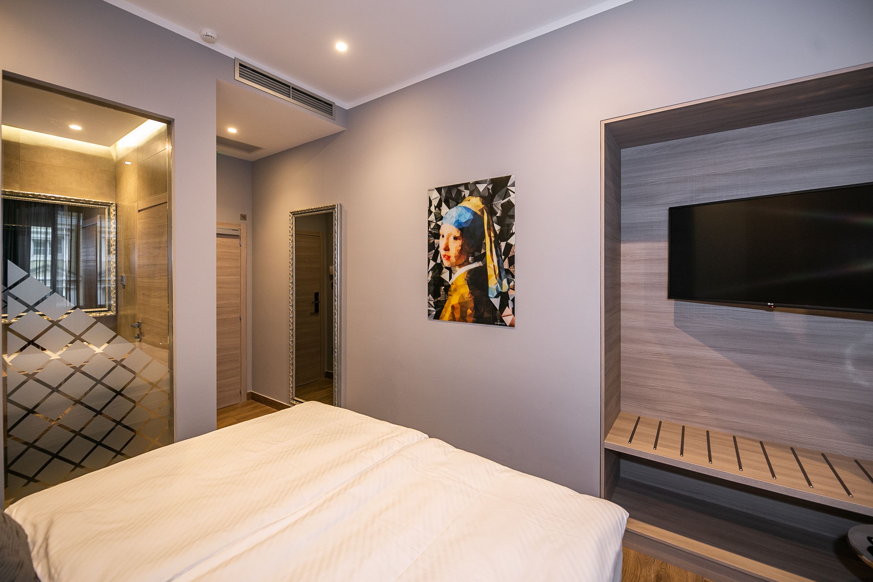 A modern hotel room with a large bed, a flat-screen TV, and a painting on the wall.
