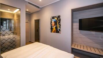 A modern hotel room with a large bed, a flat-screen TV, and a painting on the wall.