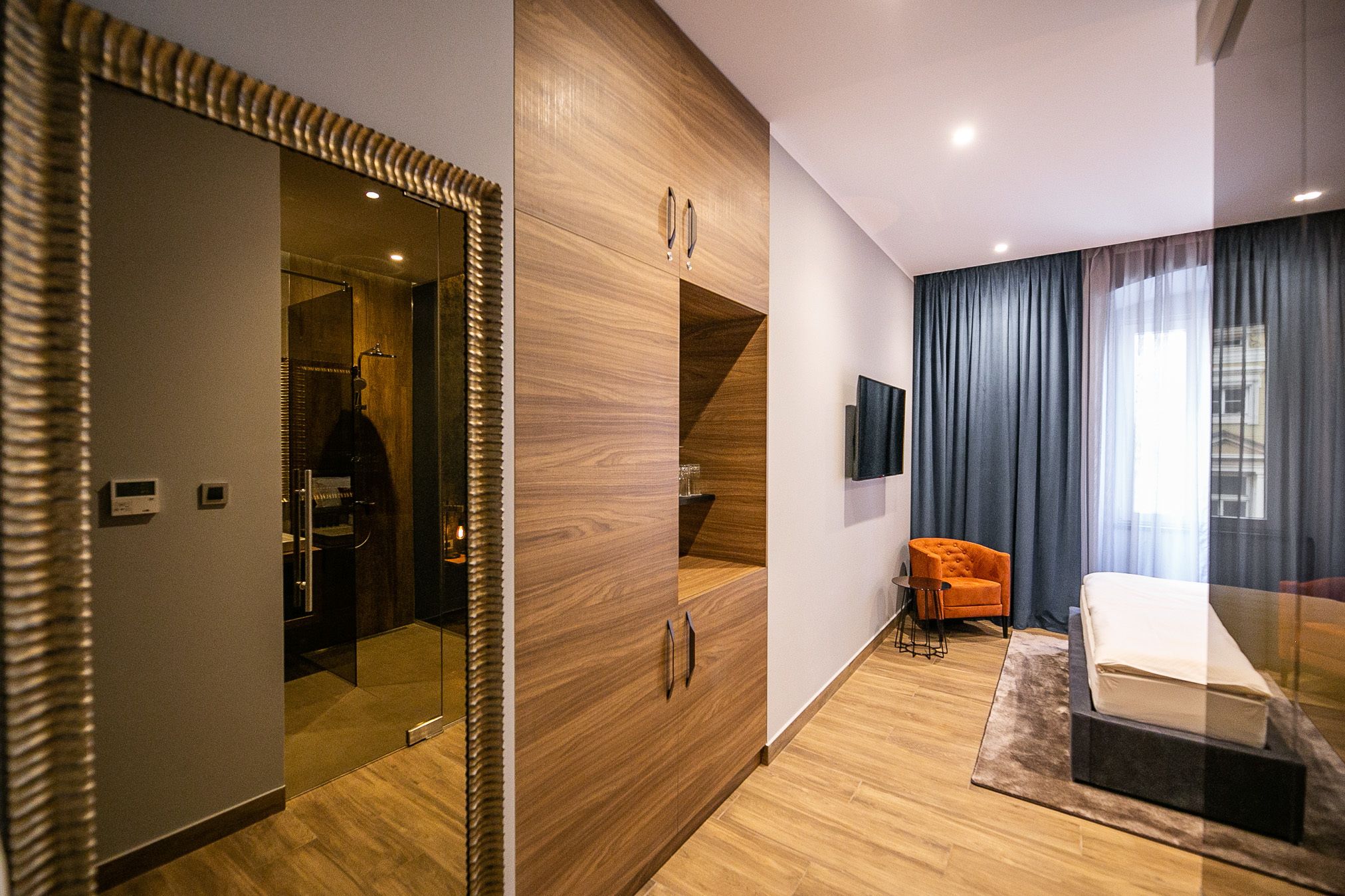 Een moderne slaapkamer met een houten garderobe, een glazen douche en een bed met een donkere hoofdbord.