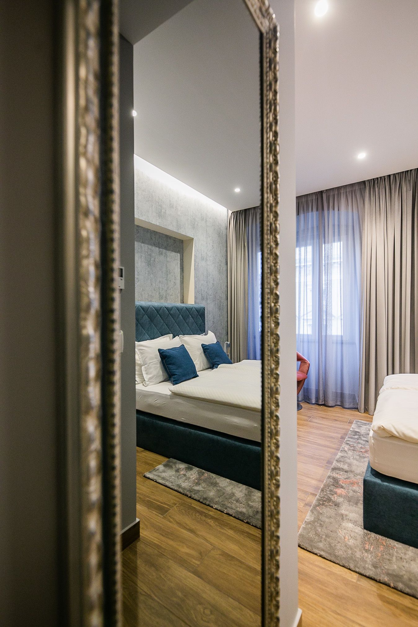 A modern bedroom with a large bed, a bedside table, and a mirror reflecting the room.