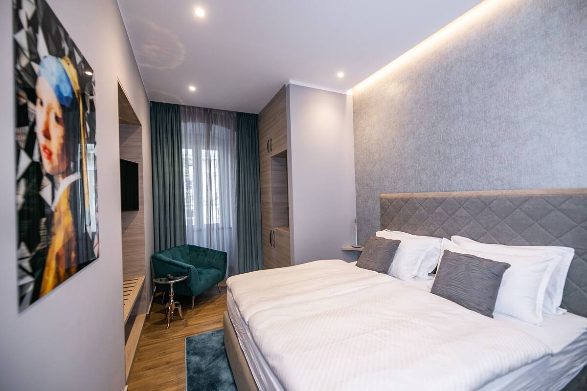Een moderne slaapkamer met een groot bed, een groene fauteuil en een schilderij aan de muur.