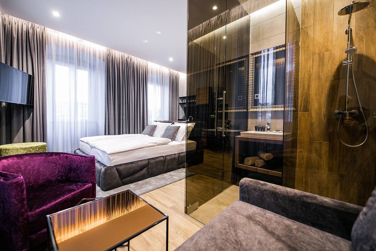 Een moderne hotelkamer met een bed, zithoek en douche.
