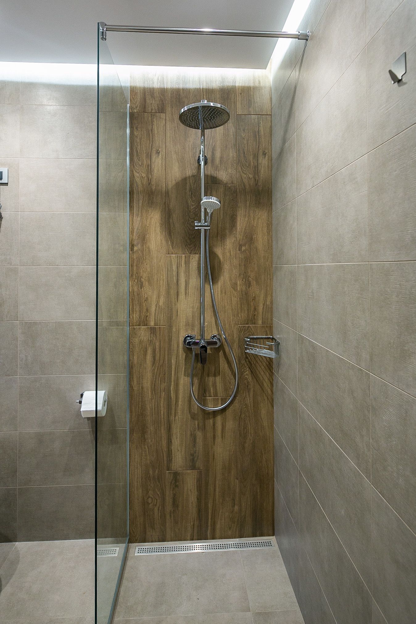 A glass-enclosed shower with a wooden panel wall, a handheld showerhead, and a wall-mounted faucet.