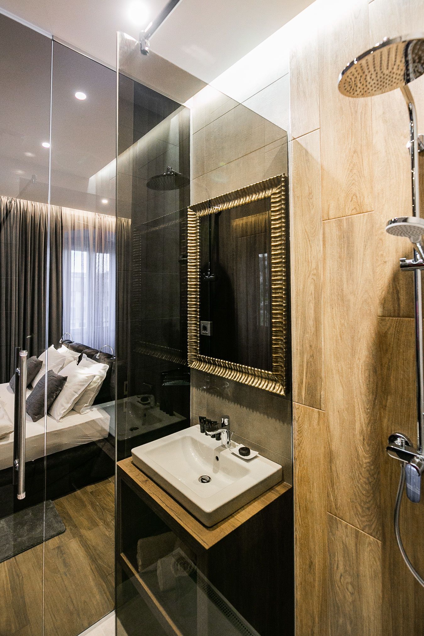 A modern bathroom with a glass-enclosed shower, a wooden vanity with a sink, and a large mirror with a gold frame.