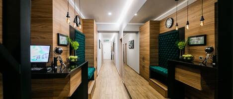 Un área de recepción con paneles de madera, un mostrador de recepción, una computadora y un banco tapizado en verde.