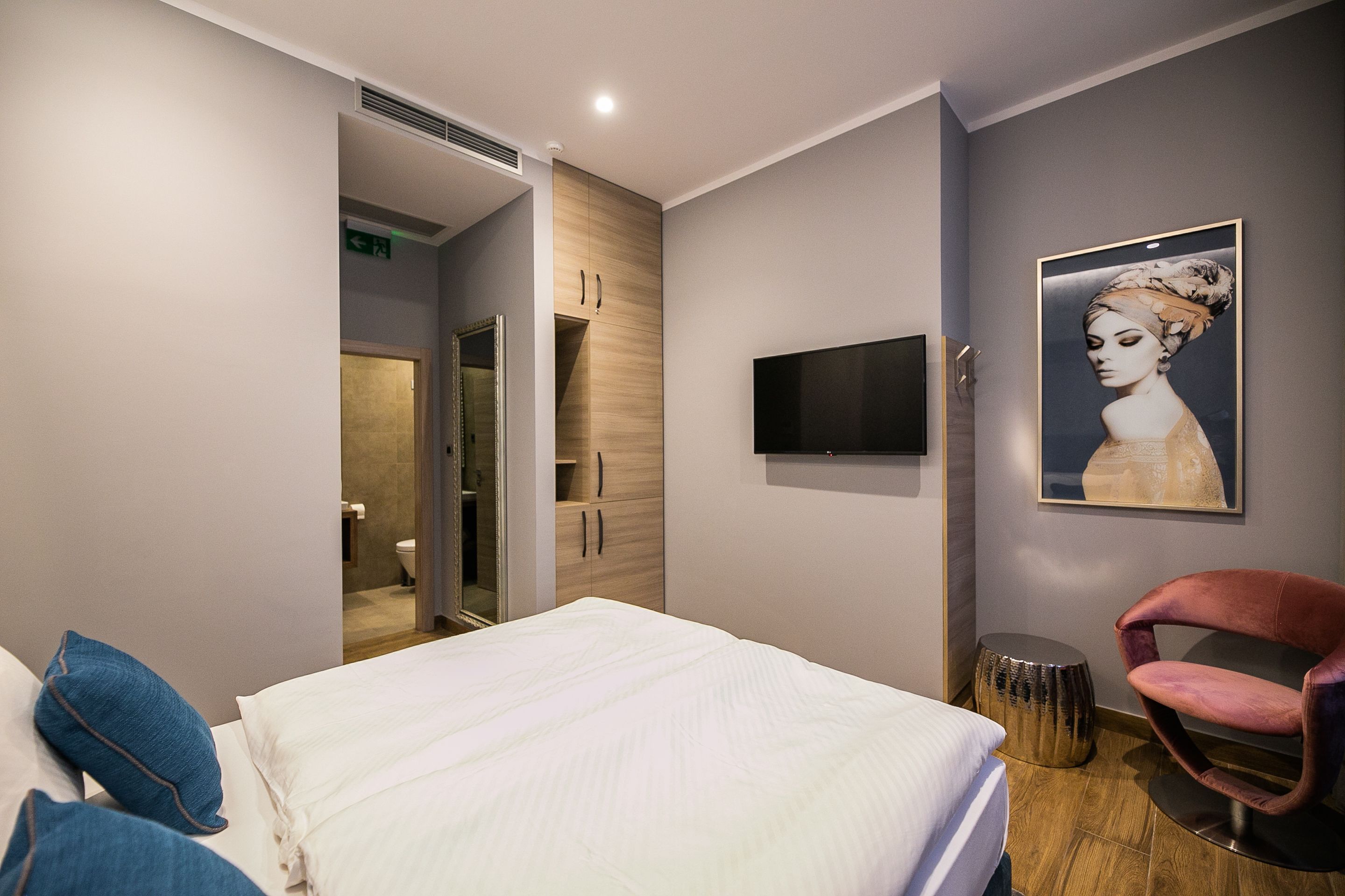 Una habitación de hotel moderna con una cama, un televisor, una obra de arte enmarcada y una silla.