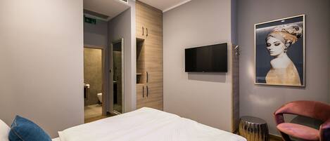 Una habitación de hotel moderna con una cama, un televisor, una obra de arte enmarcada y una silla.