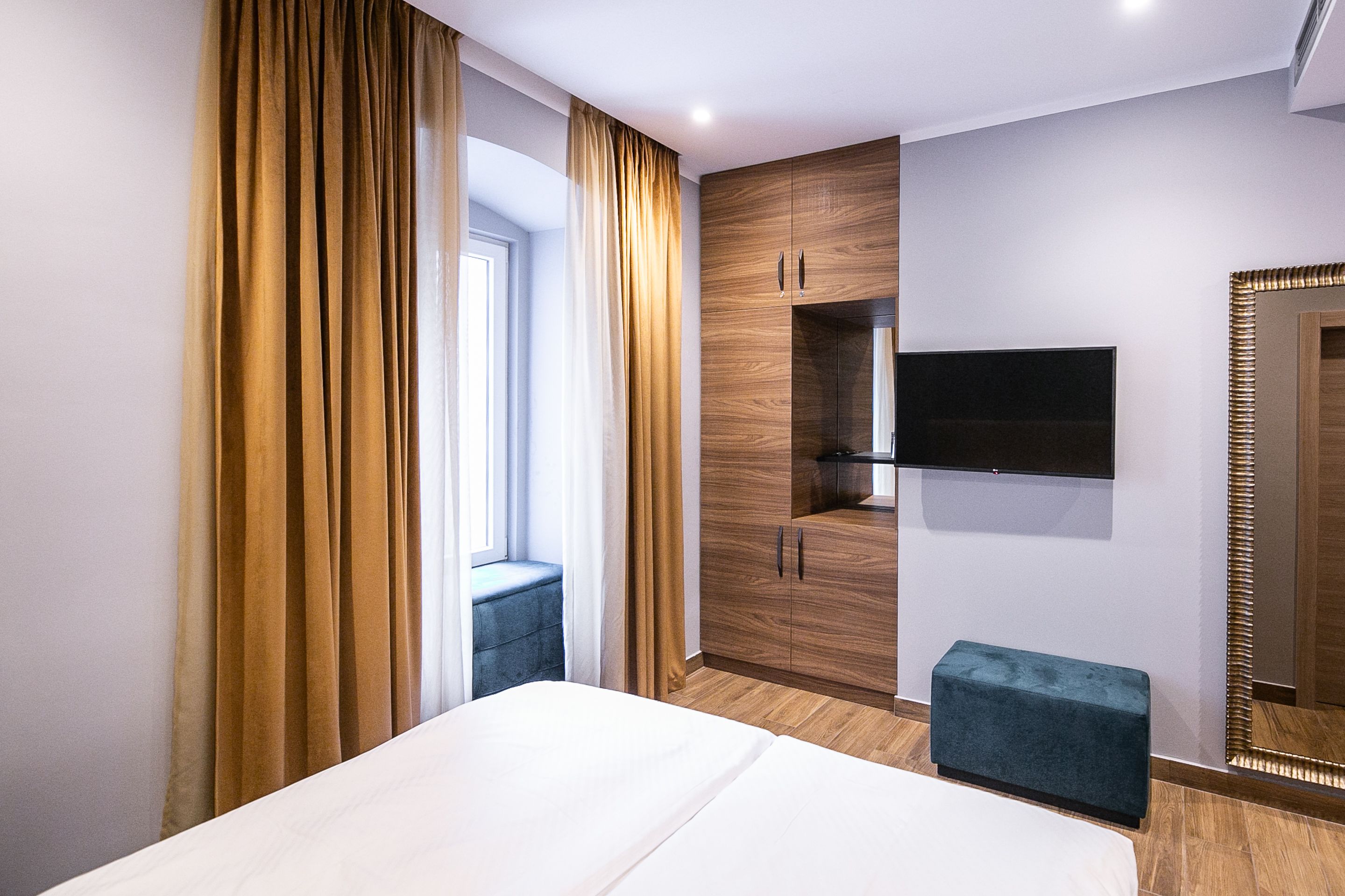 Ein modernes Hotelzimmer mit einem großen Bett, einem Kleiderschrank, einem an der Wand befestigten Fernseher und einem mit Vorhängen versehenen Fenster.